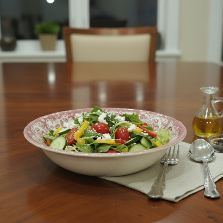 Bowl of salad on a wooden table with a bottle of oil and cutlery.