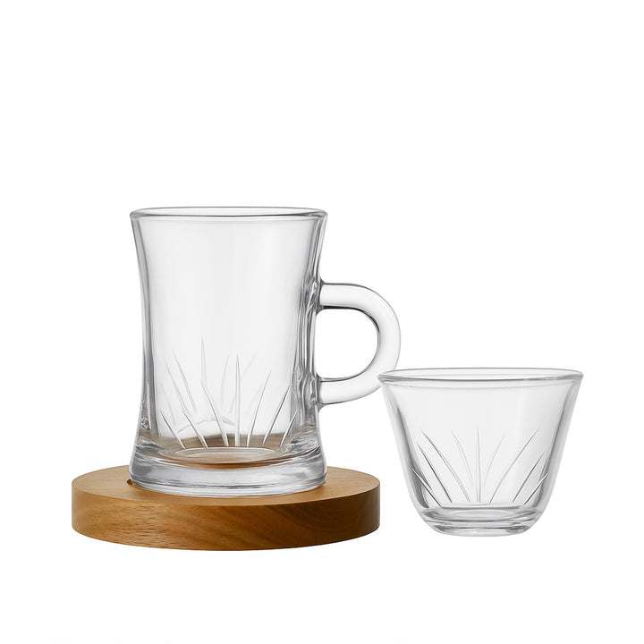 Clear glass mug with handle and smaller glass cup on a wooden coaster against a white background