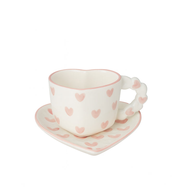 Ceramic cup and saucer with pink heart patterns on a white background