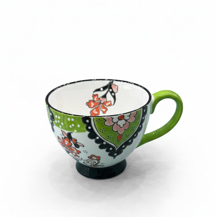 Ceramic cup with a white base finish featuring green and pink floral patterns, black detailing, and a glossy green handle — displayed on a white background from Siddiq Gifts, Mussafah Abu Dhabi.