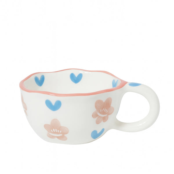 Ceramic cup with a white finish featuring blue heart and pink floral patterns, wavy rim, and rounded handle — displayed on a white background from Siddiq Gifts, Mussafah Abu Dhabi.