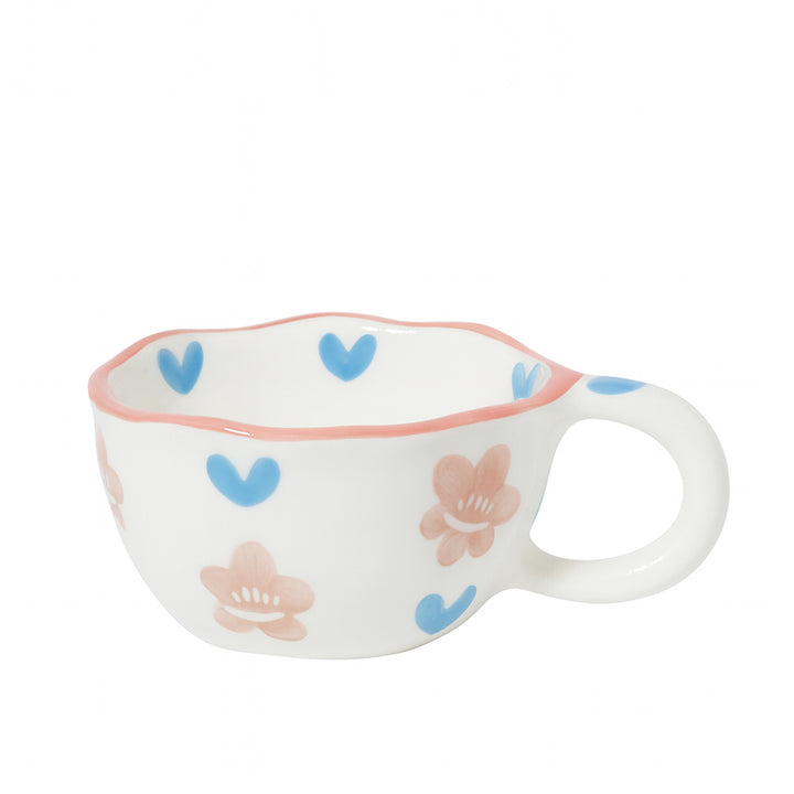 Ceramic cup with a white finish featuring blue heart and pink floral patterns, wavy rim, and rounded handle — displayed on a white background from Siddiq Gifts, Mussafah Abu Dhabi.