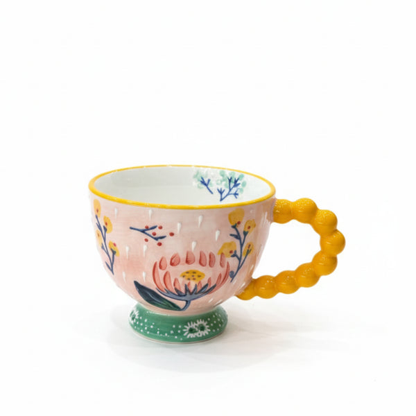 Decorative mug with floral design and yellow handle on a white background