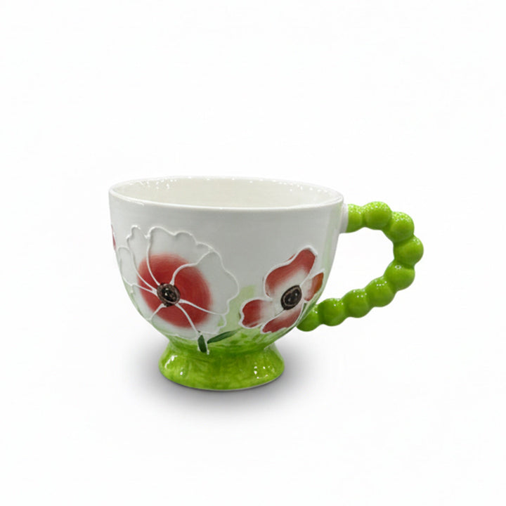Ceramic mug with floral design and green handle on a white background