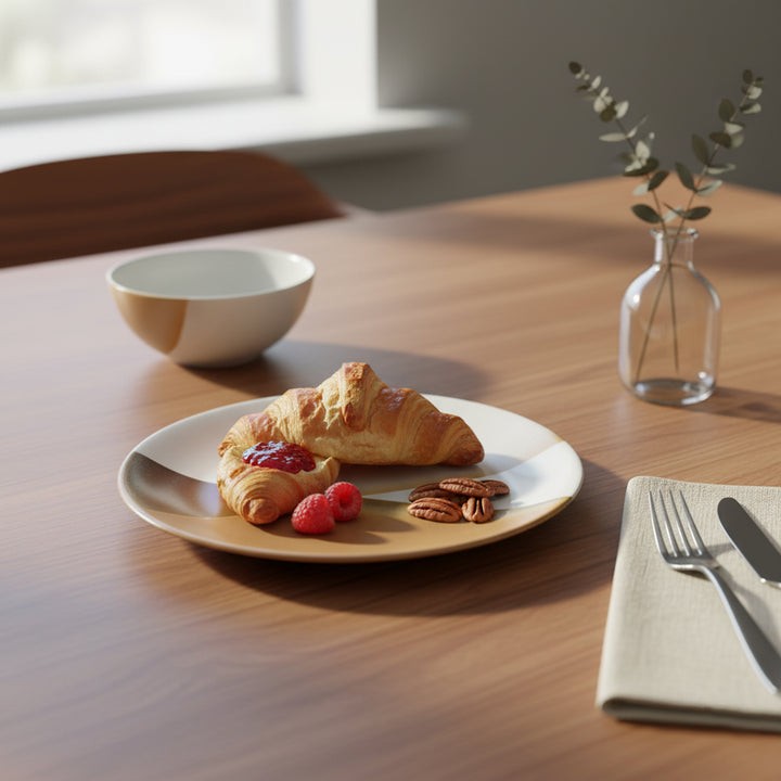 Breakfast setting with a croissant, berries, and nuts on a plate, accompanied by a bowl and vase on a wooden table.
