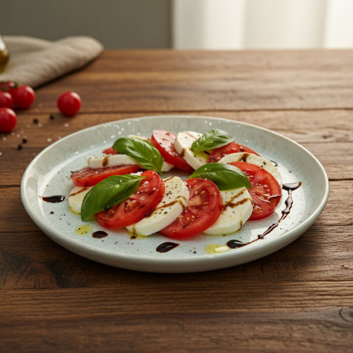 Caprese salad with tomatoes, mozzarella, and basil on a speckled plate with a wooden background.