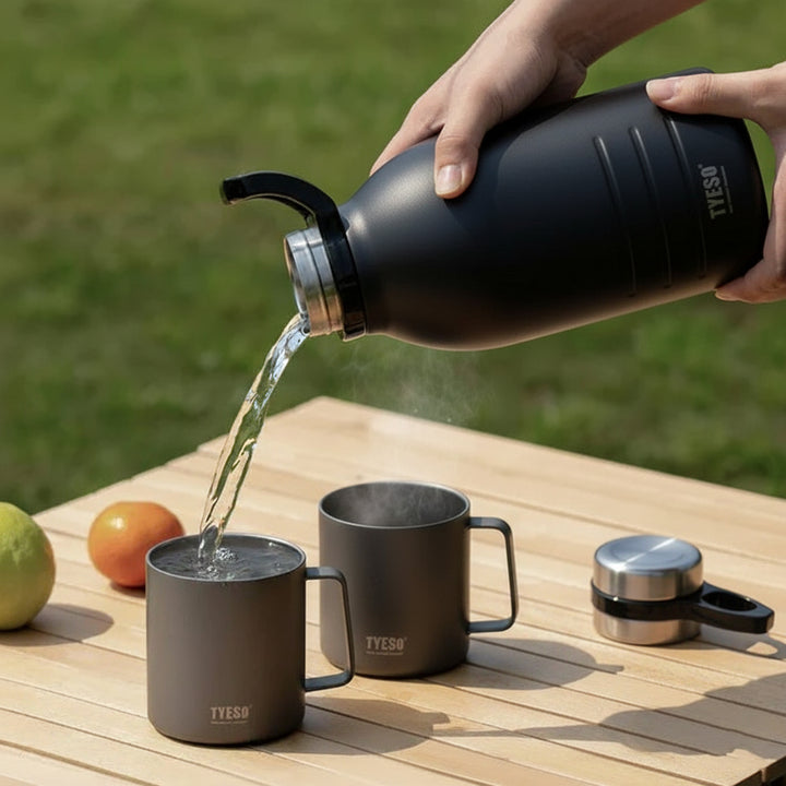 Person pouring liquid from a black YESEU bottle into two gray mugs on a wooden table outdoors.