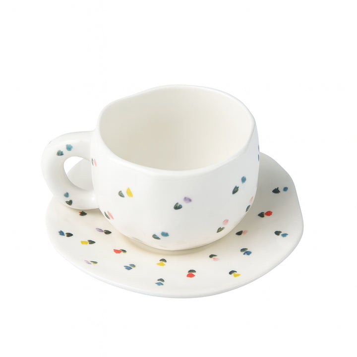 White ceramic cup and saucer with colorful polka dot pattern on a white background