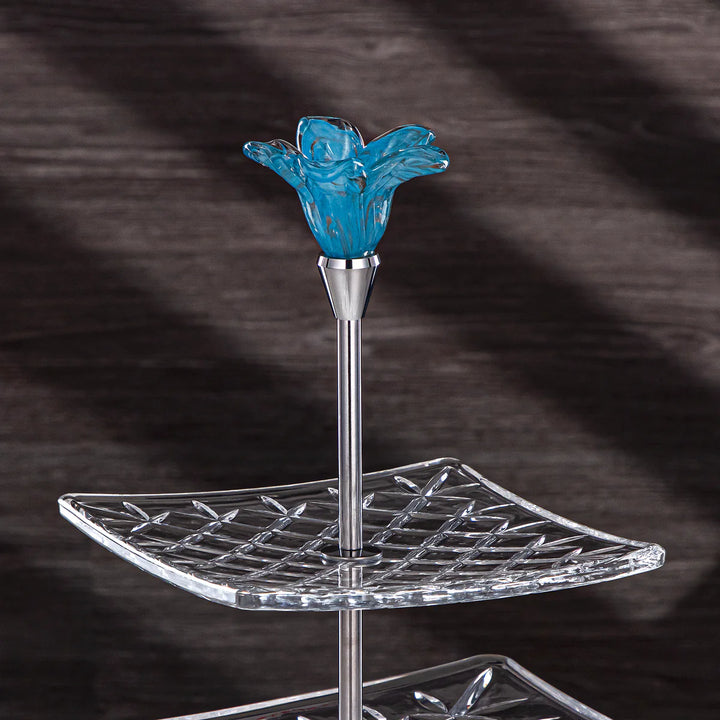 Two-tiered crystal stand with a blue glass flower on a dark background