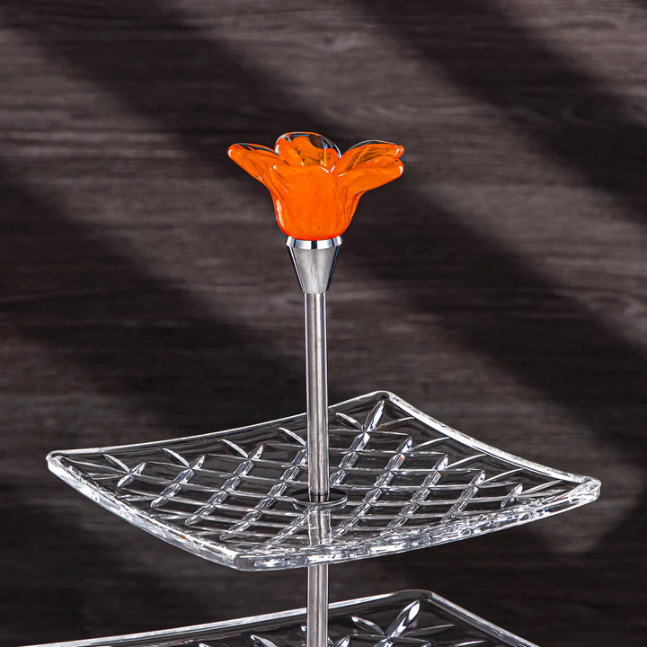 Two-tiered glass stand with an orange glass flower on a dark background