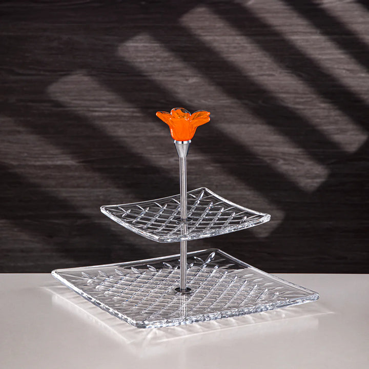 Clear glass three-tiered stand with an orange flower on a dark background