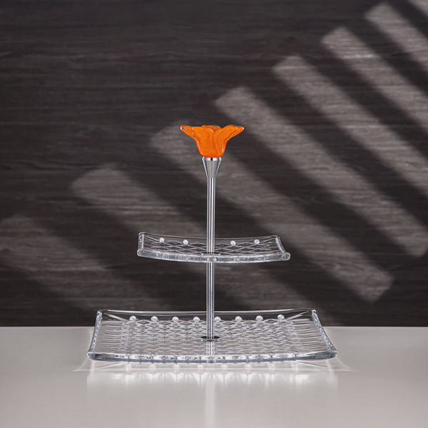 Two-tiered glass stand with an orange top on a reflective surface with a dark background