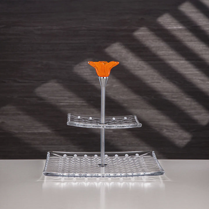 Two-tiered glass stand with an orange top on a reflective surface with a dark background