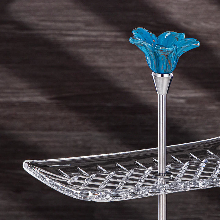 Two-tiered crystal stand with a blue glass flower on a dark background