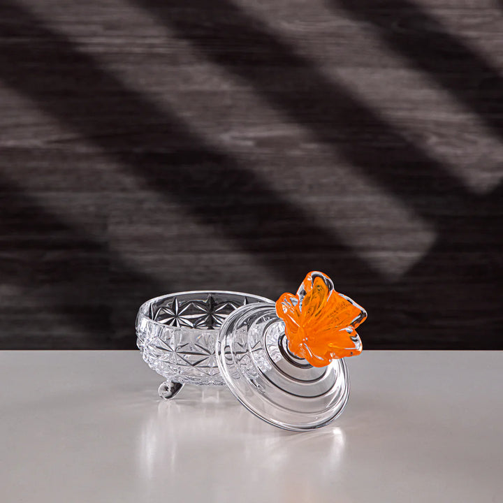 Clear glass dish with an orange flower on a gray surface and dark background