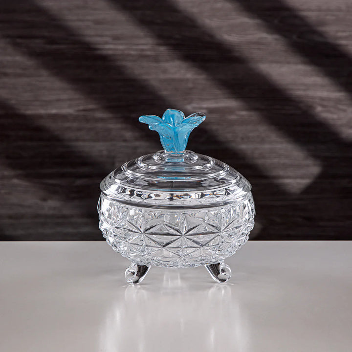 Crystal jar with a blue floral lid on a reflective surface with a striped background