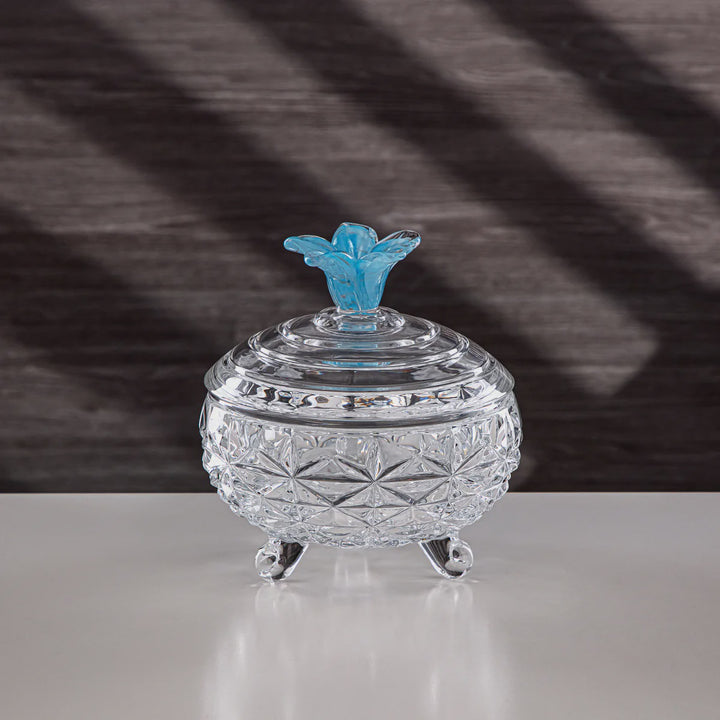 Crystal trinket dish with a blue floral lid on a reflective surface with a striped background