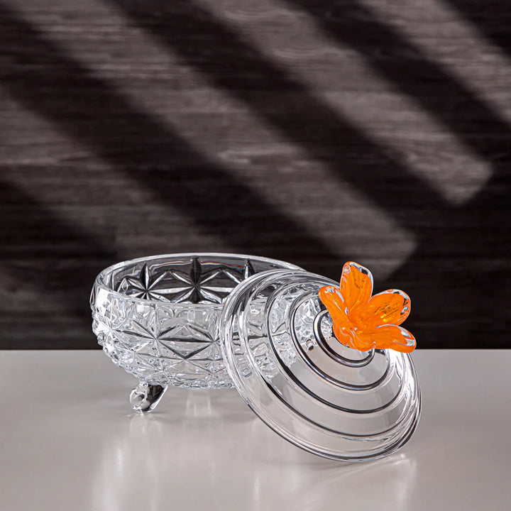 Clear glass container with a decorative lid featuring a butterfly charm on a textured surface.