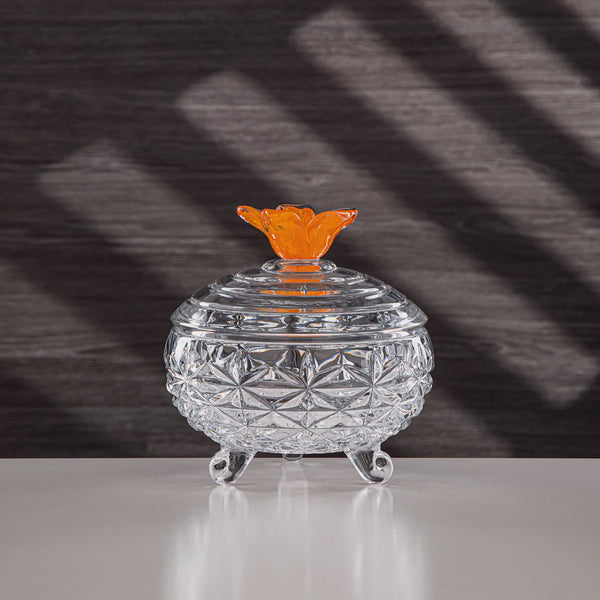 Clear glass container with an orange lid on a reflective surface and dark background