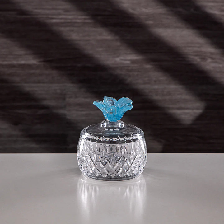 Crystal jar with a blue decorative top on a reflective surface with a striped background