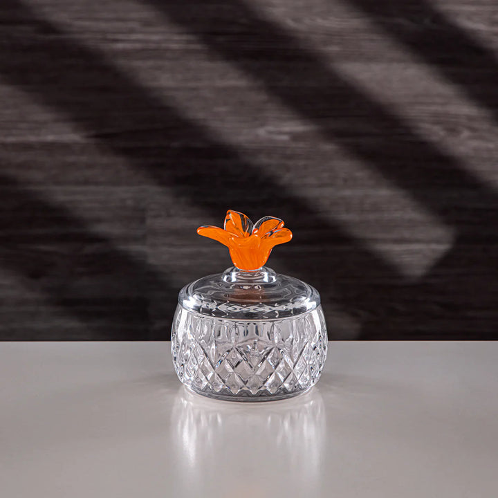 Clear glass jar with an orange lid on a reflective surface and dark textured background