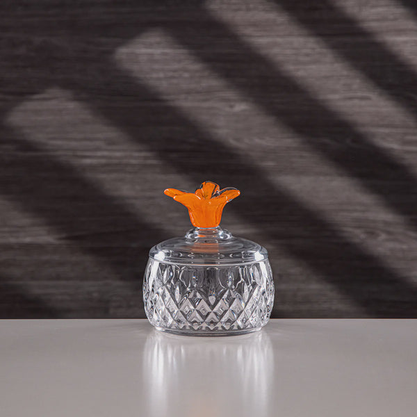 Clear glass container with an orange lid on a reflective surface, dark background