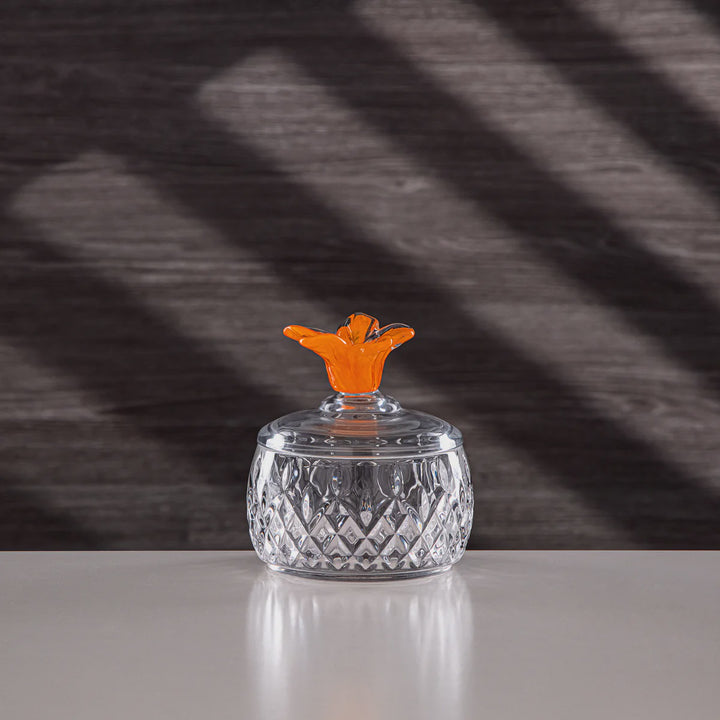 Clear glass container with an orange lid on a reflective surface, dark background