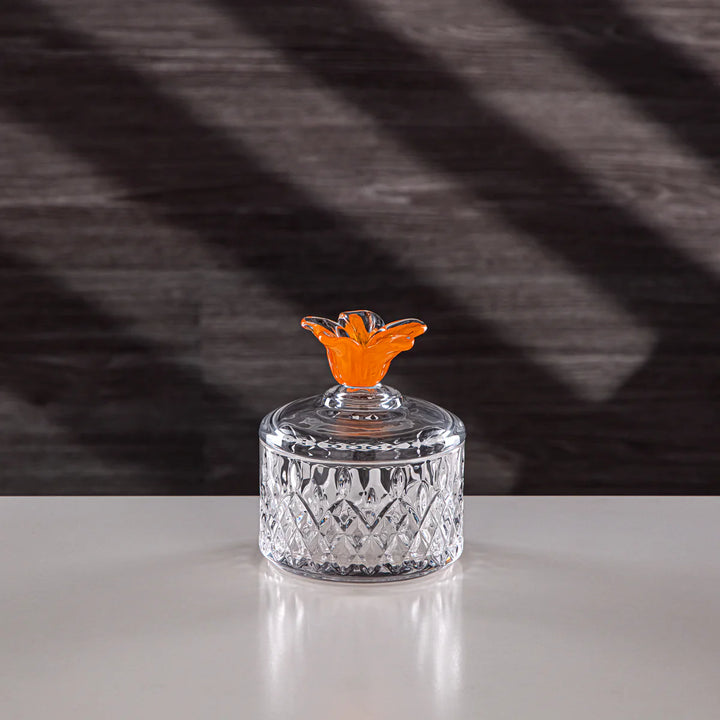 Crystal jar with an orange lid on a white surface and dark background