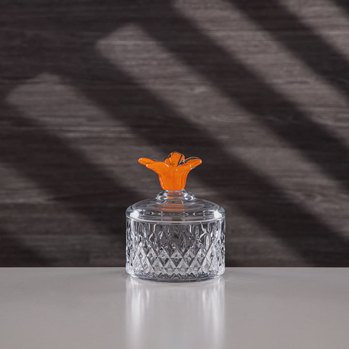 Glass container with an orange lid on a reflective surface, dark textured background