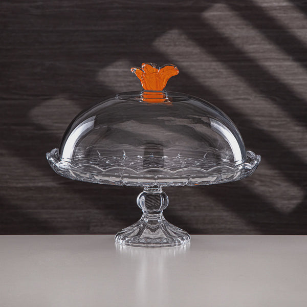 Clear glass cake stand with a decorative orange handle on a dark background