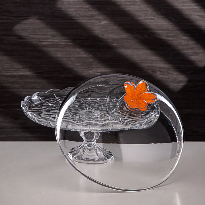 Clear glass cake stand with an orange butterfly on a black and white striped background