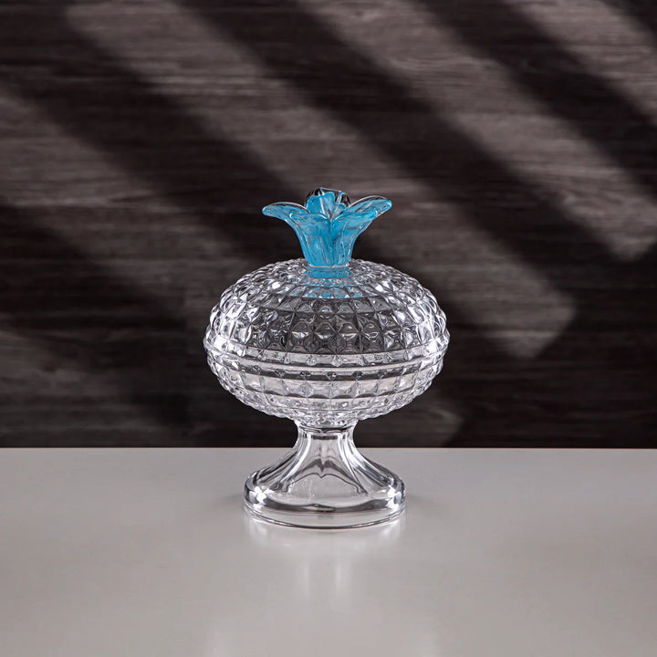 Crystal container with blue lid on a reflective surface and striped background