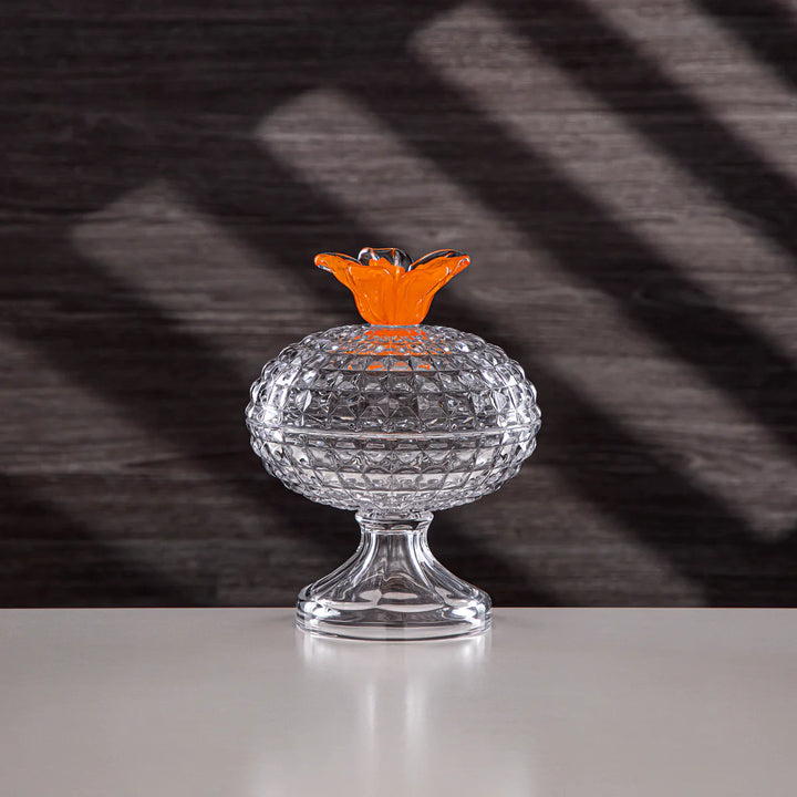 Clear glass lamp with orange shade on a reflective surface and dark textured background