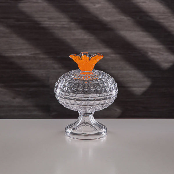 Clear glass container with an orange top on a reflective surface and dark textured background