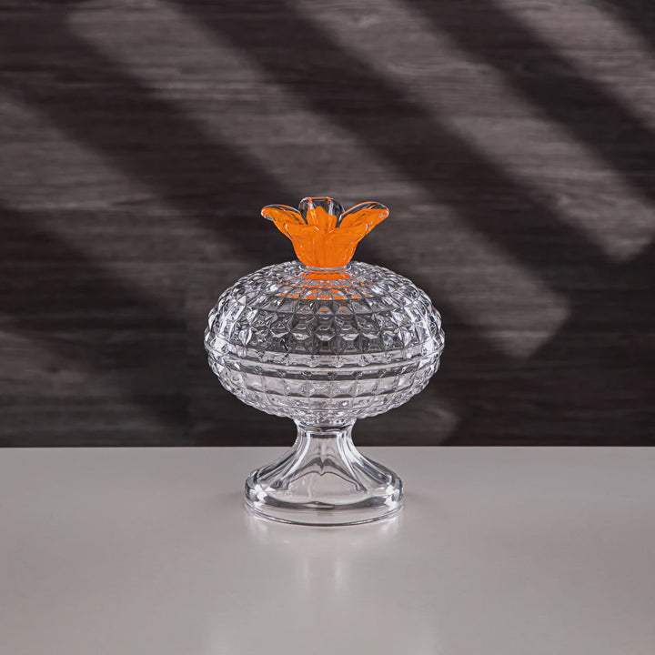 Clear glass container with an orange top on a reflective surface and dark textured background