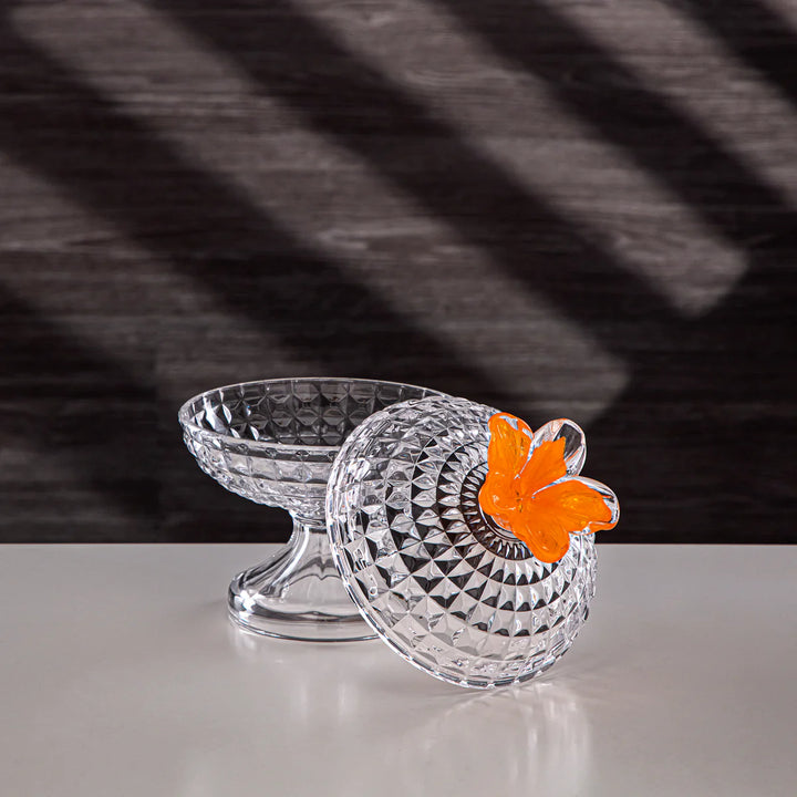 Clear glass dish with an orange flower on a reflective surface and dark background