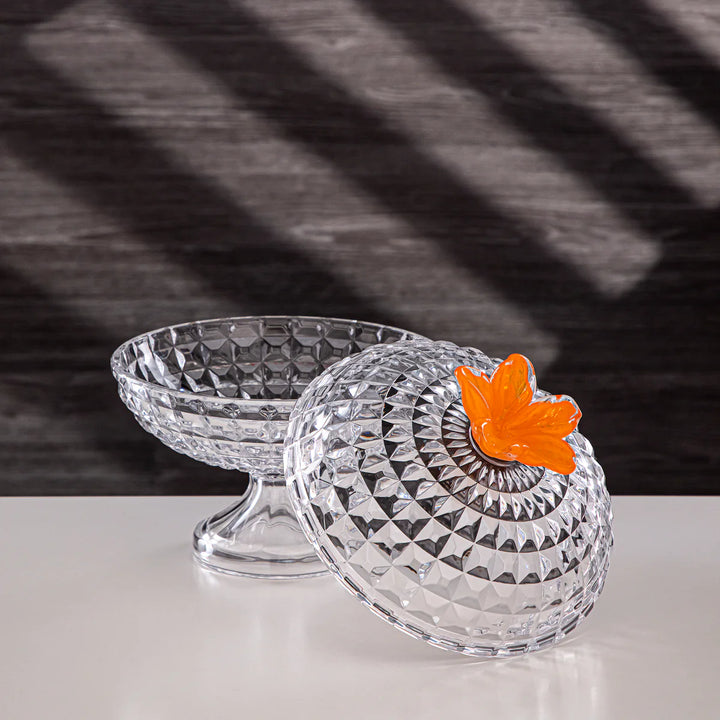 Clear glass candy dish with a decorative orange leaf on a black and white striped background