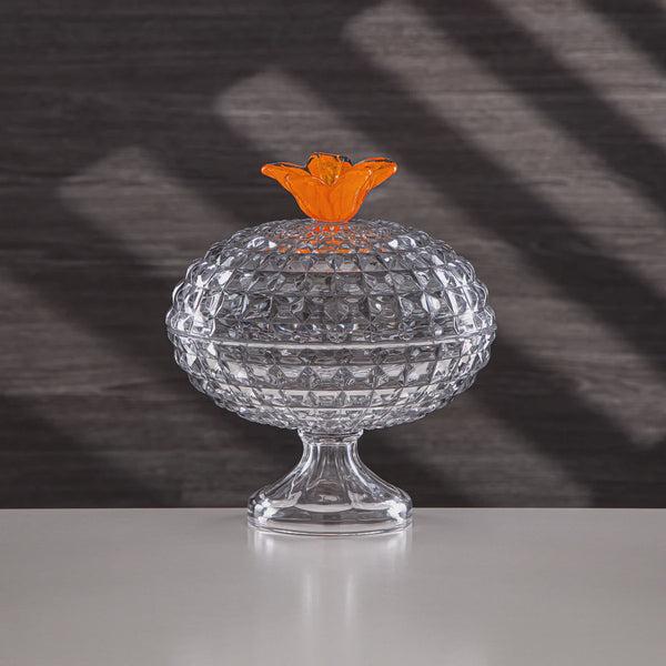 Clear glass container with an orange lid on a reflective surface and dark background