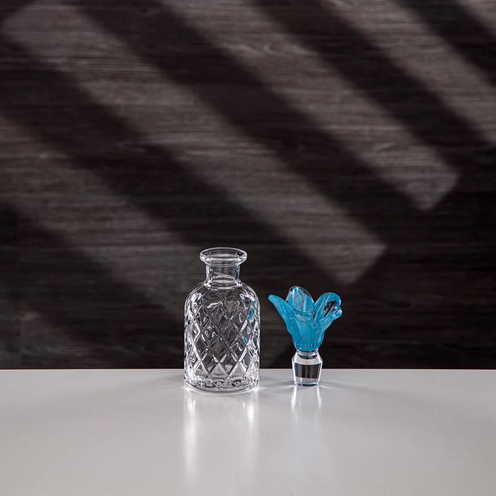 Clear glass decanter and blue glass sculpture on a white surface with a dark, textured background