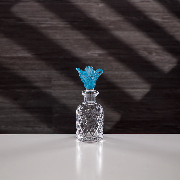 Clear glass decanter with a blue stopper on a white surface and dark background