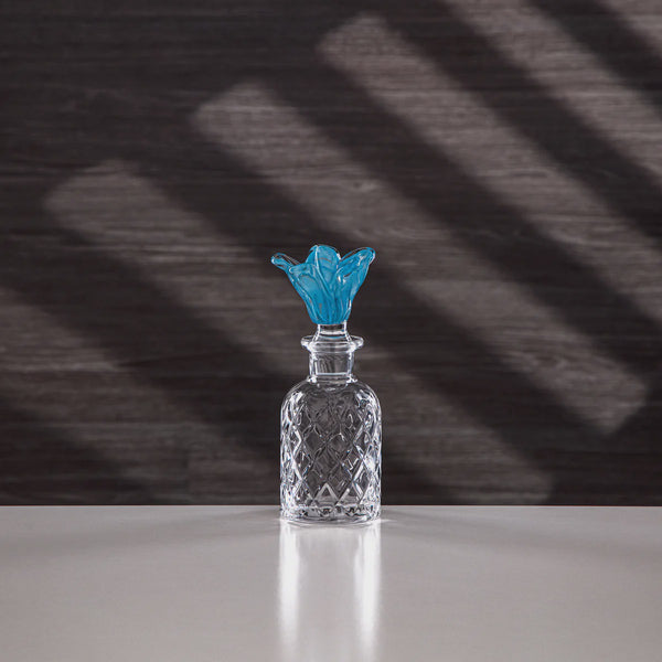 Clear glass bottle with a blue cap on a reflective surface and dark background