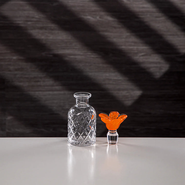 Clear glass decanter and orange glass object on a reflective surface with a dark, striped background