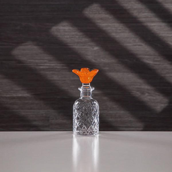 Clear glass bottle with an orange stopper on a dark background