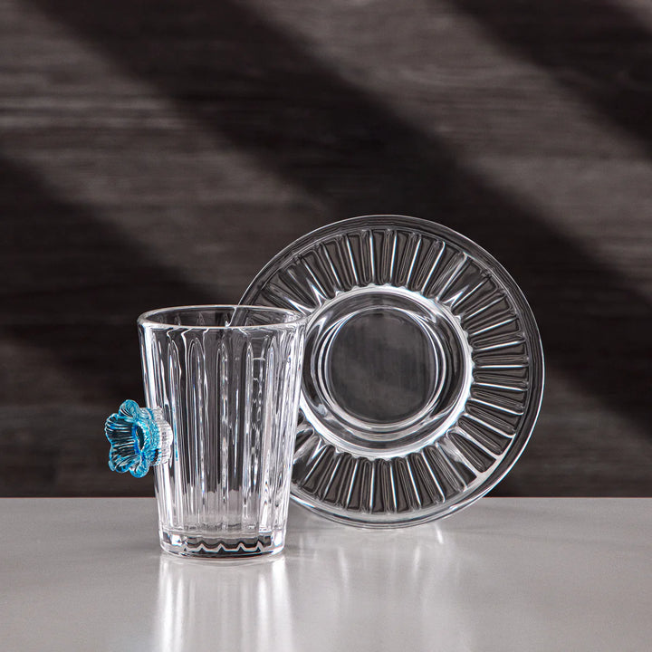 Clear glass tumbler and plate with decorative blue element on a dark background