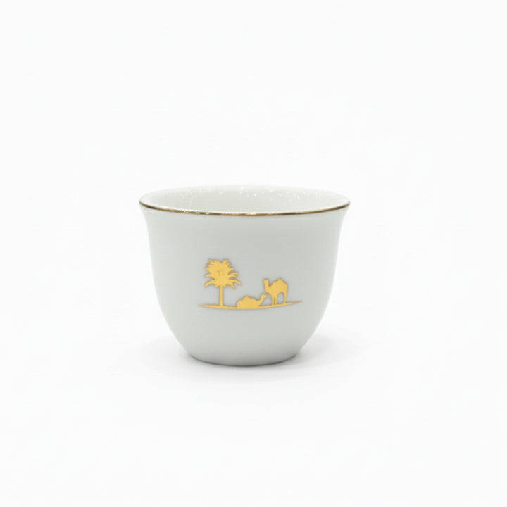 White ceramic cup with gold rim and desert scene design on a white background