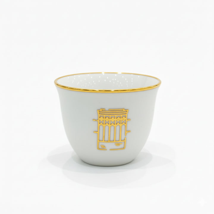 White ceramic cup with gold rim and geometric design on a white background