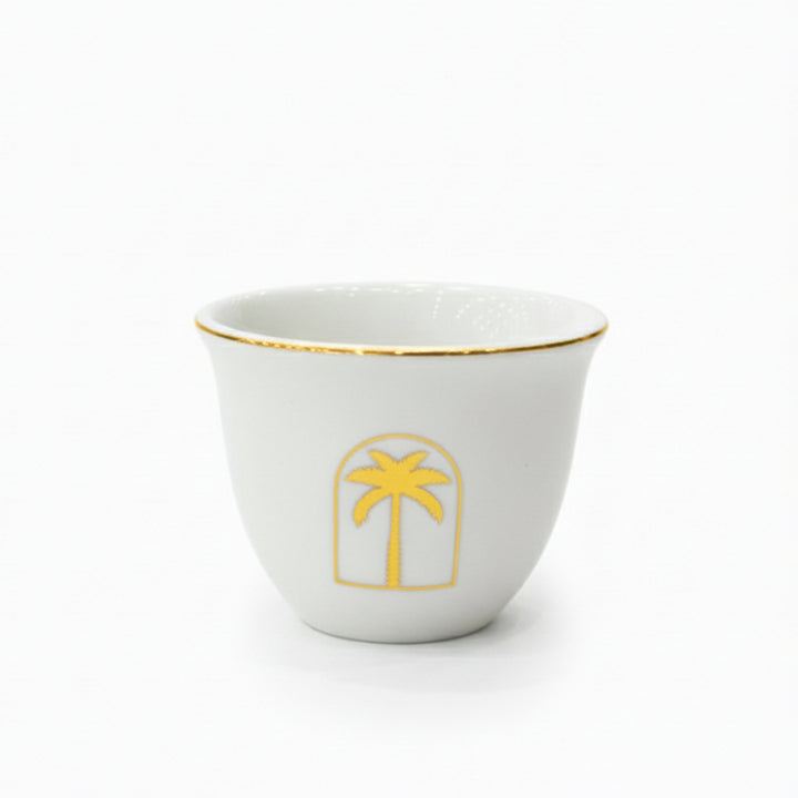 White cup with gold rim and palm tree design on a white background