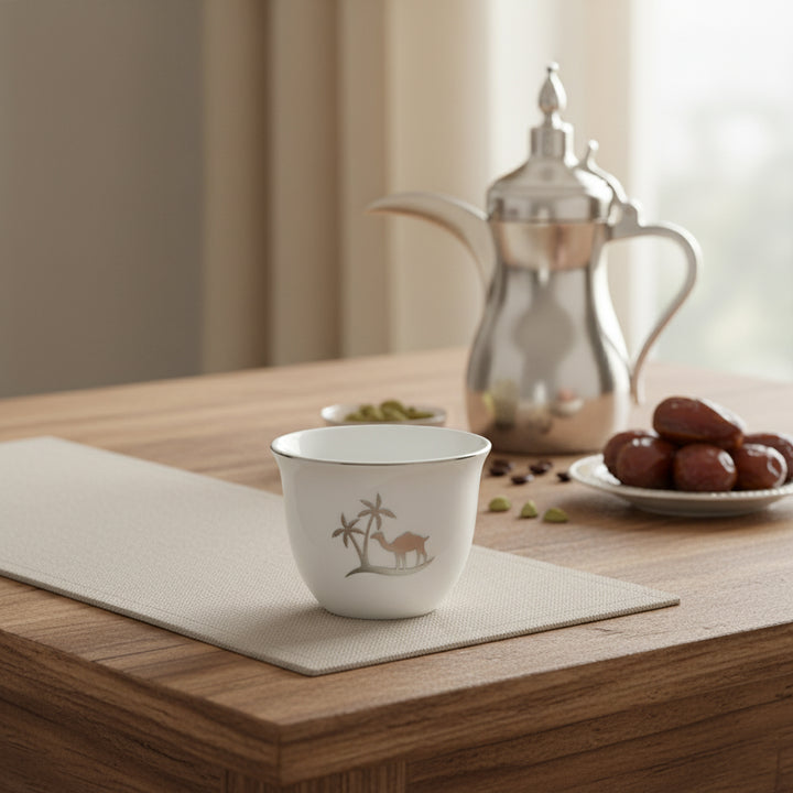 White teacup with a design on a wooden table with a silver teapot and dates in the background.