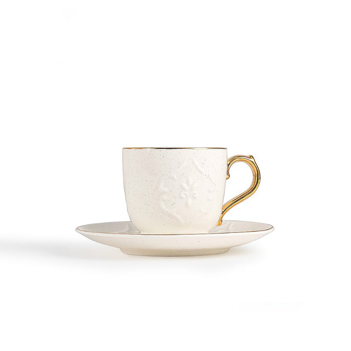 White ceramic cup with gold handle and saucer on a white background