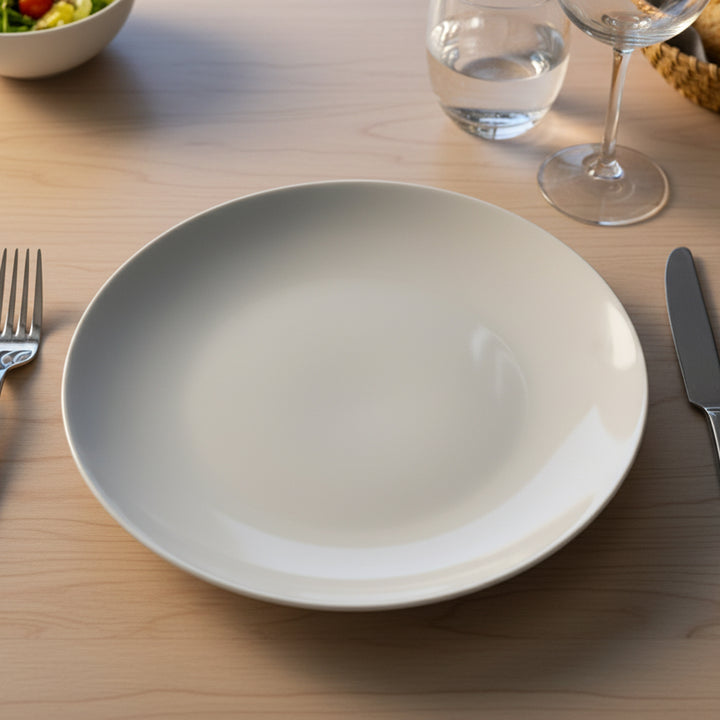 White plate on a wooden table with cutlery and glasses in the background
